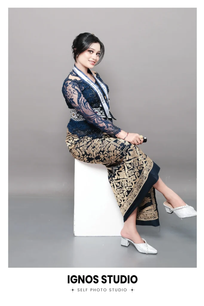 Wanita mengenakan kebaya biru modern dan kain batik berpose duduk di Ignos Studio.